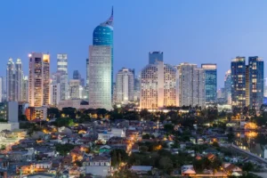 The Jakarta skyline at dusk features lit skyscrapers rising above a densely populated residential area in Indonesia.