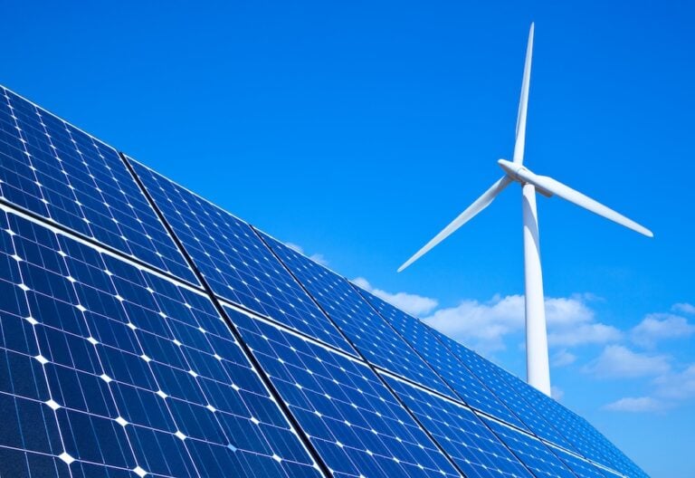 Solar panels and wind turbine against blue sky