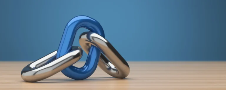 A glossy blue chain link is interlocked with two silver metallic links on a wooden table against a solid blue background.