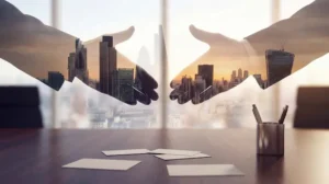 Two hands reaching for a handshake are overlaid with a city skyline in a double exposure above a conference table.