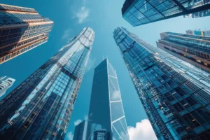 A low-angle view shows glass financial skyscrapers towering into a bright blue sky above the city downtown.