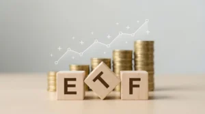 Wooden blocks spelling ETF sit in front of stacked gold coins with a rising growth line overlay