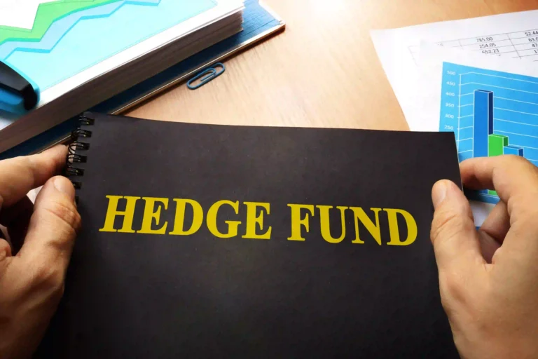 A person's hands hold open a black notebook displaying the text HEDGE FUND in yellow next to financial charts.
