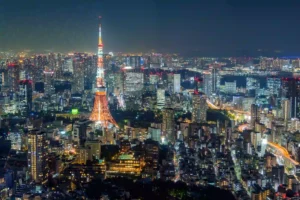 The illuminated red and white Tokyo Tower stands out against the vast, glowing city lights of Tokyo at night.