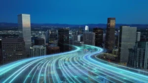 Glowing blue digital light streams wind through a city skyline at dusk beside illuminated modern skyscrapers.