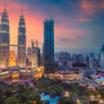 The illuminated Petronas Twin Towers stand tall over the Kuala Lumpur city skyline and park at sunset.