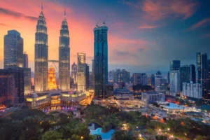 The illuminated Petronas Twin Towers stand tall over the Kuala Lumpur city skyline and park at sunset.