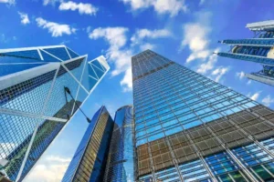 Modern glass skyscrapers including the Bank of China Tower rise upward against a bright blue sky in Hong Kong Central.