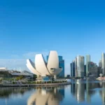Marina Bay Sands, the ArtScience Museum, and downtown skyscrapers reflect across calm waterfront waters in Singapore.