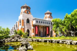 The twin octagonal towers of Aletheia University Grand Chapel rise behind a green rock-bordered pond under a clear sky.