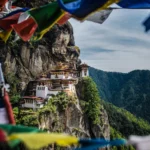 Colorful prayer flags frame Paro Taktsang, the cliffside Tiger's Nest monastery perched high above a forested valley in Bhutan.