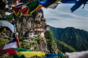 Colorful prayer flags frame Paro Taktsang, the cliffside Tiger's Nest monastery perched high above a forested valley in Bhutan.