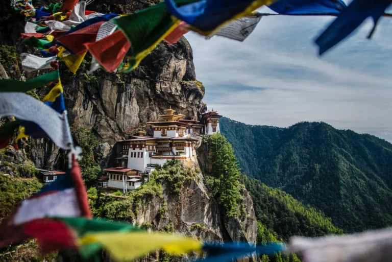 Colorful prayer flags frame Paro Taktsang, the cliffside Tiger's Nest monastery perched high above a forested valley in Bhutan.
