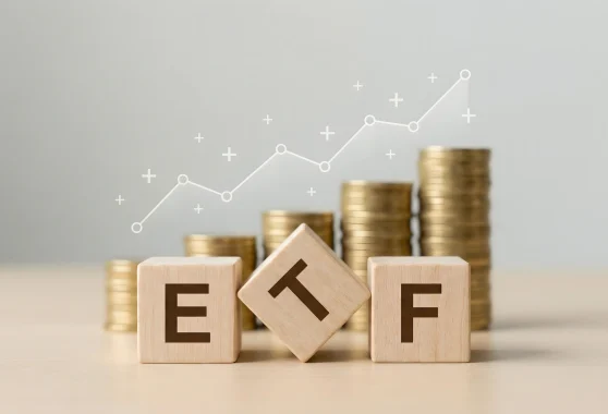 Wooden blocks spelling ETF sit in front of stacked gold coins with a rising growth line overlay