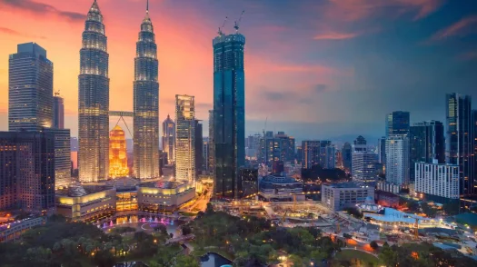 The illuminated Petronas Twin Towers stand tall over the Kuala Lumpur city skyline and park at sunset.