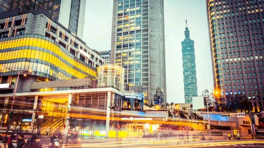 Traffic light trails streak past modern Taipei skyscrapers with Taipei 101 standing in the background.