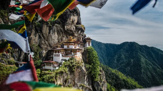 Colorful prayer flags frame Paro Taktsang, the cliffside Tiger's Nest monastery perched high above a forested valley in Bhutan.
